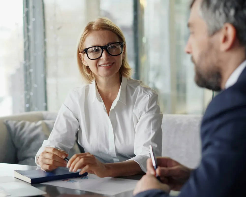 Professional in glasses meeting with a client across a table in a bright office